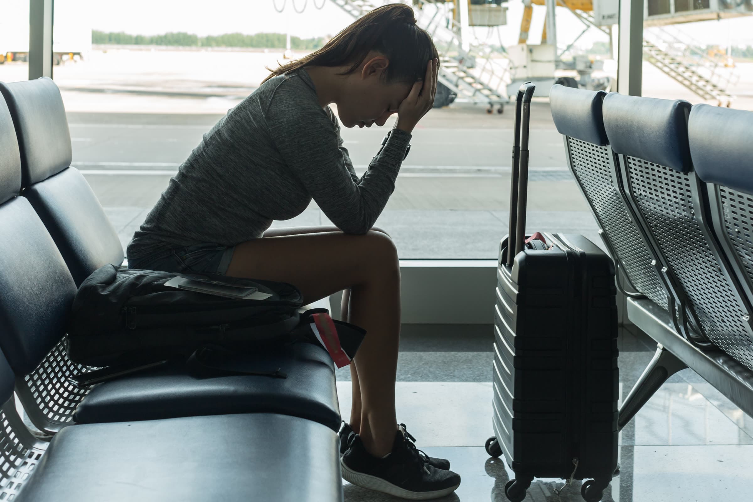 A traveller sitting alone in an airport waiting area with her head in her hand